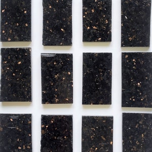 May include: A set of twelve black and gold square tiles with a speckled pattern. The tiles are arranged in three rows of four.