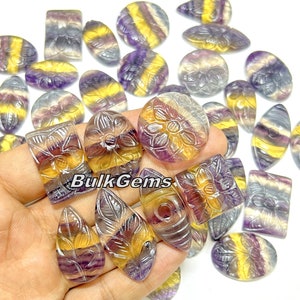 Può includere: Una collezione di 20 cabochon di fluorite intagliati a forma di pietra preziosa, di varie forme e dimensioni. I cabochon sono un mix di colori viola, giallo e bianco con intricati disegni floreali e di foglie.
