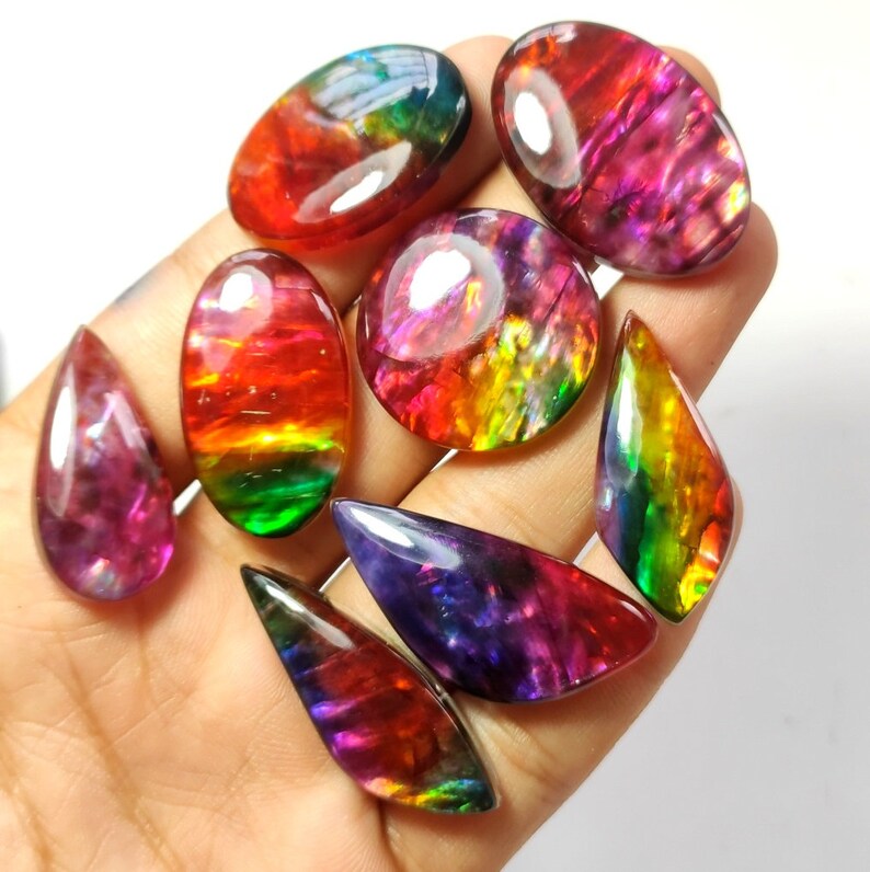 May include: A collection of seven iridescent gemstone cabochons in various shapes and sizes. The stones display a rainbow of colours, including red, orange, yellow, green, blue, and purple.