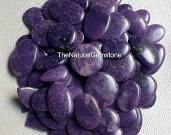 May include: A large pile of purple lepidolite cabochons, smooth and polished, with a speckled appearance. TheNaturalGemstone is printed on a white label in the center of the image.