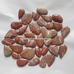 May include: A collection of 25 natural red and white banded agate cabochons, each with a unique pattern. The cabochons are in various shapes, including teardrop and oval. TheNaturalGemstone is printed on the image.
