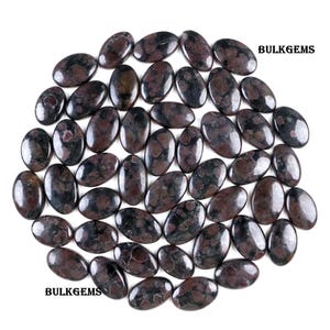 Peut inclure: Collection de pierres précieuses ovales, de couleurs rouge foncé et noire, disposées de près. Les pierres précieuses ont un aspect poli et brillant. Le texte "BULKGEMS" est visible en haut à droite et en bas à gauche.