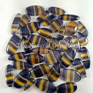 May include: A collection of 25 natural gemstone cabochons in a variety of shapes and sizes. The cabochons are a mix of purple, yellow, and white colors with a striped pattern. The cabochons are all polished and have a smooth, glossy finish.
