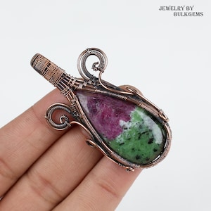 May include: A teardrop-shaped green and pink gemstone pendant wrapped in copper wire. The pendant is set in a wire-wrapped design with intricate details.