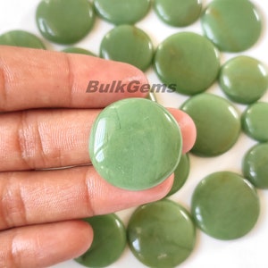 May include: A close-up of a hand holding a smooth, green, round stone. The stone is polished and has a slight sheen. There are many other similar stones in the background.