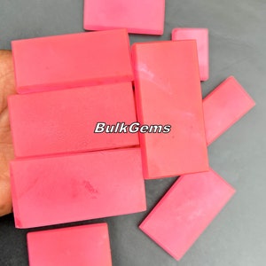 May include: A collection of eight pink rectangular cabochons, likely for jewelry making, with the text "BulkGems" printed on one of the stones.