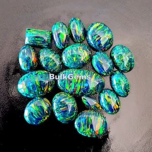 May include: A collection of 14 oval-shaped green and blue opal gemstones with iridescent flashes of color. The stones are arranged in a cluster on a black background. BulkGems is printed on the image.