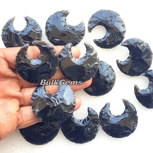 May include: Ten black obsidian crescent moon shaped arrowheads. The arrowheads are smooth and polished with a glossy finish.