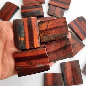May include: A collection of red tiger's eye gemstone slices. The slices are rectangular and have a natural, polished finish. The red tiger's eye has a distinctive chatoyancy, which is a shimmering effect that appears when the stone is turned in the light.