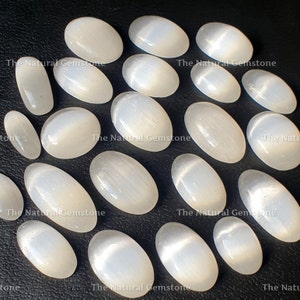 May include: A collection of 18 white oval selenite stones with a shimmering, iridescent effect. The stones are arranged in a circle on a black surface.