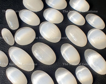 May include: A collection of 18 white oval selenite stones with a shimmering, iridescent effect. The stones are arranged in a circle on a black surface.
