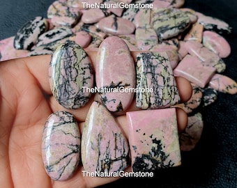 Puede incluir: Una colección de cabujones de piedra preciosa con patrones rosa y negro. Los cabujones son de varias formas y tamaños, incluyendo ovalados, en forma de lágrima y rectangulares. TheNaturalGemstone está impreso en la imagen.