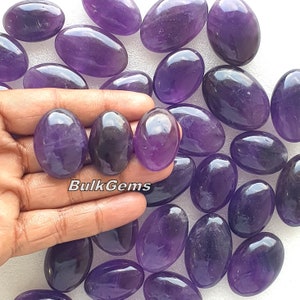 Könnte beinhalten: Eine Sammlung glatter, polierter Amethyststeine in verschiedenen Violetttönen. Die Steine sind oval geformt und haben eine glänzende Oberfläche. Der Text "BulkGems" ist im Bild sichtbar.