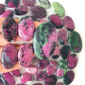 May include: A collection of oval-shaped green, pink, and black gemstones. The stones are smooth and polished, and they have a variety of patterns and colours. BulkGems is printed on the image.