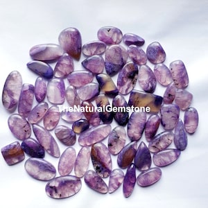 Puede incluir: Una colección de 40 cabujones de piedras preciosas naturales de color púrpura y amarillo. Los cabujones son de varias formas y tamaños, con un acabado liso y pulido. TheNaturalGemstone está impreso en la imagen.