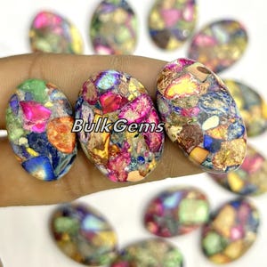 May include: A collection of oval-shaped, multi-colored, polished gemstones. The stones have a speckled pattern of blue, green, red, orange, yellow, and brown.