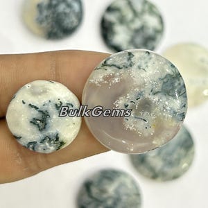 May include: Assortment of round, polished moss agate cabochons. The cabochons are white with green and gray dendritic patterns. The cabochons are approximately 1 inch in diameter.