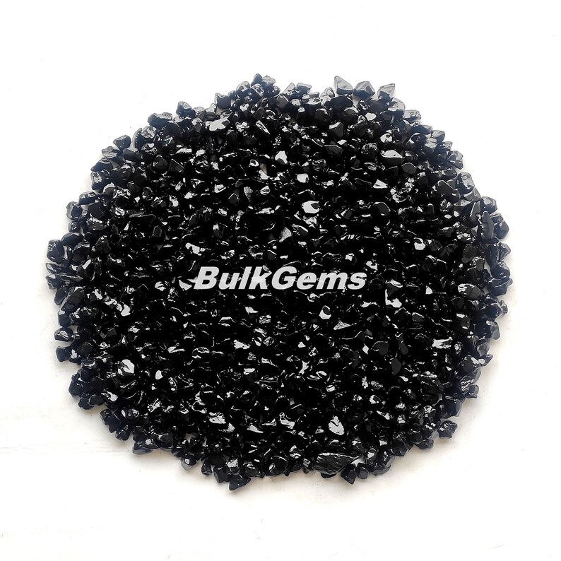 May include: A close-up of a pile of black obsidian chips. The chips are small and irregular in shape, and they have a shiny, glassy finish.