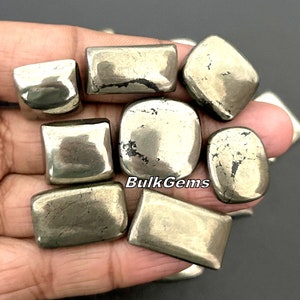Könnte beinhalten: Eine Sammlung von acht Pyrit-Steinen, jeder mit einer einzigartigen Form und Größe. Die Steine sind in einer metallischen Goldfarbe mit einer leicht rauen Textur. Die Steine sind in einer Hand angeordnet, wobei der Text "BulkGems" in der Mitte des Bildes sichtbar ist.