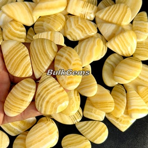 May include: A collection of yellow and white banded agate cabochons, each with a unique pattern. The cabochons are smooth and polished, and they have a pear shape. BulkGems is printed on the image.