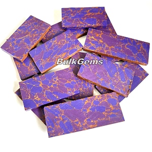 May include: A pile of purple and gold marbled stone slabs. The slabs are rectangular and have a smooth, polished finish. BulkGems is printed on the slabs.