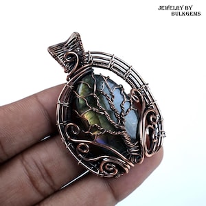 Puede incluir: Colgante artesanal de alambre de cobre con una piedra preciosa de labradorita. El colgante tiene un diseño de árbol de la vida, con la piedra preciosa en el centro. El colgante mide aproximadamente 5 cm de largo y 4 cm de ancho.