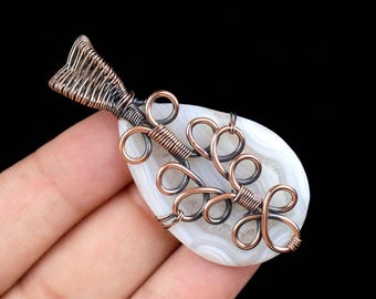 May include: A white agate pendant with a copper and silver wire wrap design. The wire wrap features intricate loops and swirls.