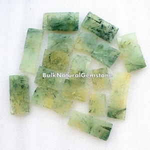 May include: A collection of green and clear, rectangular, natural gemstone pieces. The pieces are translucent and have a striated pattern. BulkNaturalGemstone is printed on the image.
