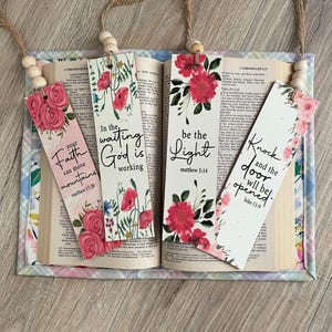 May include: Four floral bookmarks with inspirational quotes and bible verses. The bookmarks feature pink flowers, green leaves, and white backgrounds. The quotes are "In the waiting God is working", "Your faith can move mountains", "Be the light", and "Knock and the door will be opened".