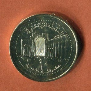 May include: A silver coin featuring a building and Arabic text. The building is a large, ornate structure with a central archway. The text is in a circular band around the edge of the coin.