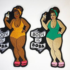 May include: Two embroidered iron-on patches featuring a cartoon woman in a swimsuit holding a boba tea. The patches are black and white with the text "Body by Boba" in a banner.