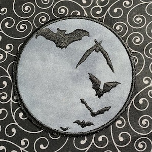 May include: A grey felt patch with a black embroidered design of a full moon and five bats flying around it.