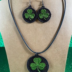 May include: A black necklace with a green shamrock pendant and matching earrings. The shamrocks are embroidered on black circles.