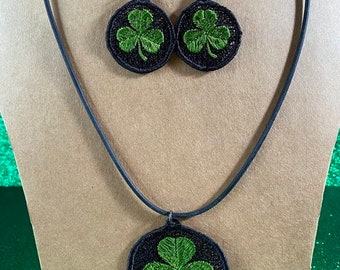 May include: A black necklace with a green shamrock pendant and matching earrings. The shamrocks are embroidered on black circles.