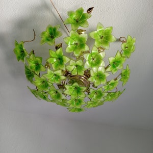 以下が含まれることがあります： 緑色の花びら型のシェードが多数ある装飾的なシーリングライト。 金色の金属フレームがあり、天井から吊り下げられています。 ライトシェードは鮮やかな緑色で、花の模様を作り出しています。