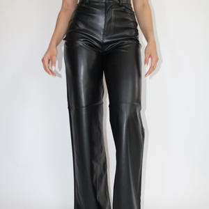May include: Black wide-leg pants made of faux leather. The pants have a high waist and a straight leg.