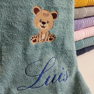 Könnte beinhalten: Ein türkisfarbenes Kapuzenhandtuch mit einem gestickten braunen Teddybär und dem Namen "Luis" in blauer Stickerei.