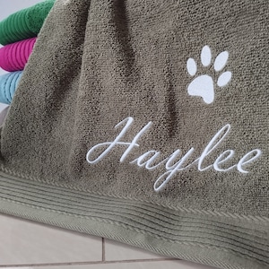 Könnte beinhalten: Ein grünes Handtuch mit einem weißen Pfotenabdruck und dem Namen "Haylee" bestickt.