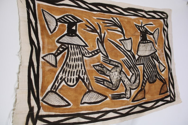 May include: A brown and black textile wall hanging with a geometric design featuring three figures. The figures are stylized and have large heads and bodies. The background is a light brown color.