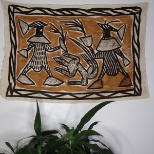 May include: A brown and white tapestry with a geometric design featuring two figures with hats and a stylized animal in the center.