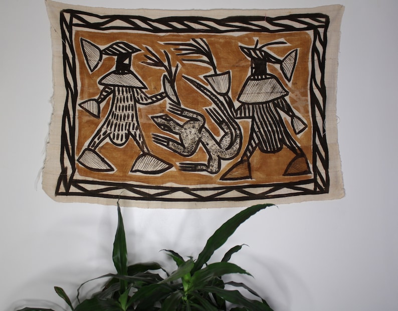 May include: A brown and white tapestry with a geometric design featuring two figures with hats and a stylized animal in the center.