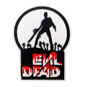 Op de afbeelding: Zwarte en witte geborduurde patch met een silhouet van een persoon die een kettingzaag vasthoudt, staand boven een groep uitgestrekte handen. De tekst "Evil Dead" is geschreven in rode en witte letters met druppels bloed.