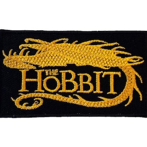 May include: A black embroidered patch with a gold dragon and the text "The Hobbit" in a stylized font.