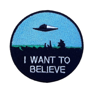Può includere: Una toppa ricamata nera e blu con un UFO che vola sopra un campo verde e il testo "I WANT TO BELIEVE".