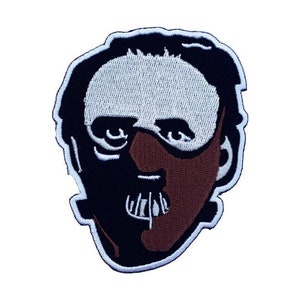 Op de afbeelding: Gestikt patch met een zwart-witte illustratie van een persoon die een bruin masker draagt met een witte mond en ogen. Het masker heeft een zwarte band om het hoofd.