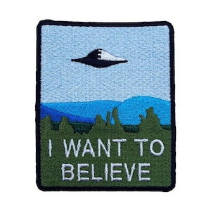 May include: A green and blue embroidered patch with a black UFO flying over a green and blue landscape. The text "I WANT TO BELIEVE" is embroidered in white on the patch.