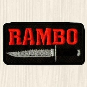 Könnte beinhalten: Schwarzer gestickter Aufnäher mit dem Wort "RAMBO" in roten Buchstaben und einem silbernen Messer mit schwarzem Griff.