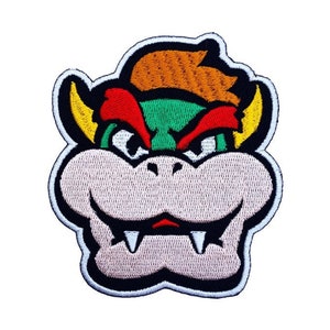 May include: Embroidered patch featuring a cartoon face of Bowser, a character from the Super Mario Bros. video game series. Bowser has a green face, red eyebrows, yellow horns, and a white mouth with sharp teeth.