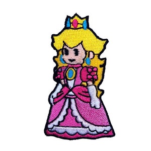 May include: An embroidered iron-on patch featuring a cartoon illustration of Princess Peach from the Super Mario video game series. She is wearing a pink dress with a white lace trim and a crown. Her hair is blonde and she has blue eyes.