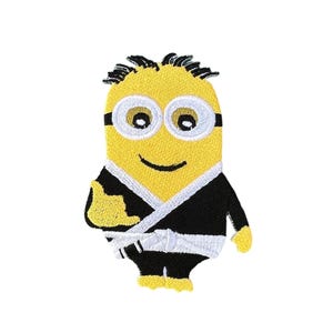 May include: A yellow minion wearing a black karate uniform with a white belt. The minion has black hair, black goggles, and a big smile.